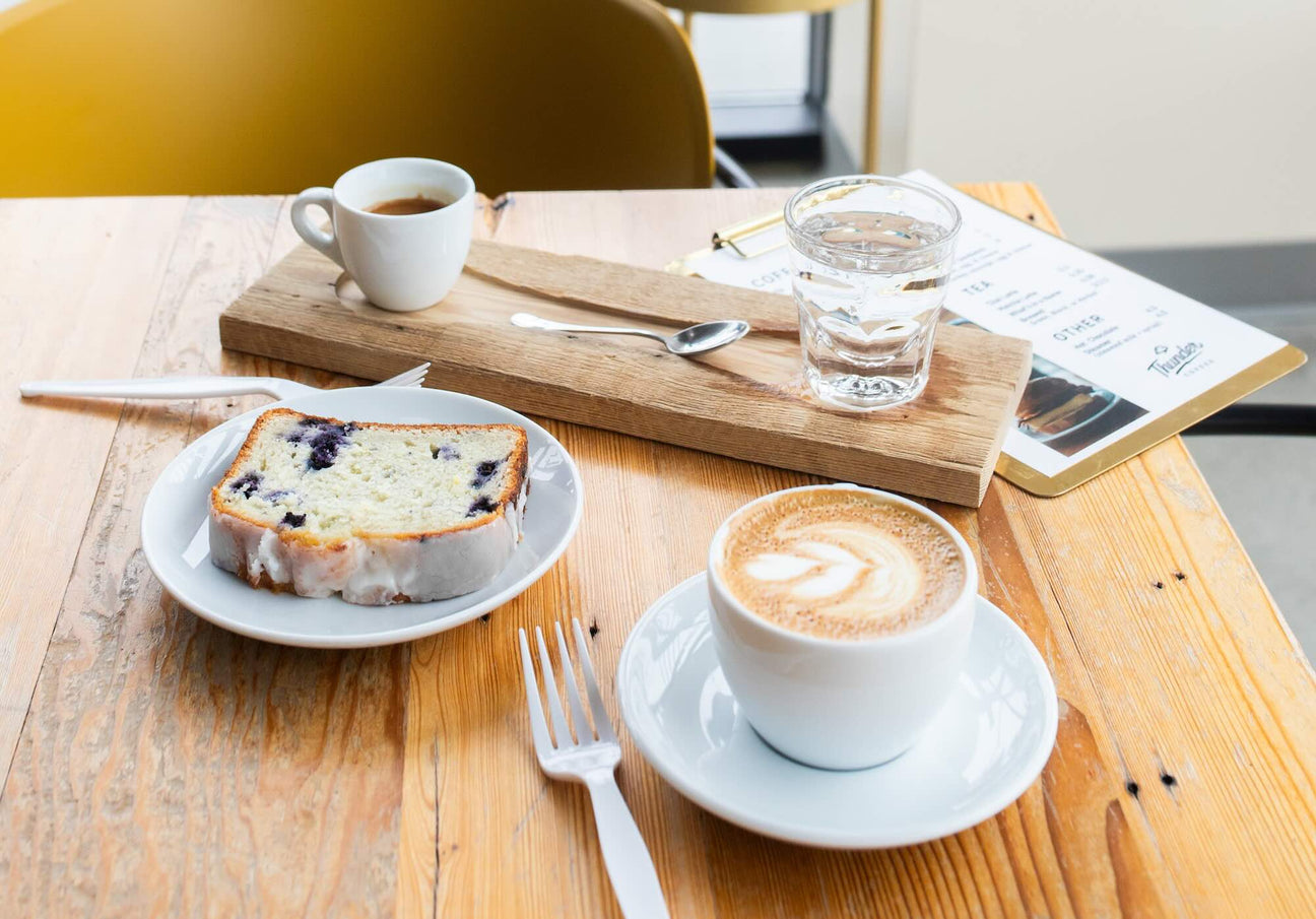 cappuccino, blueberry bread, and an espresso displayed on a cafe table